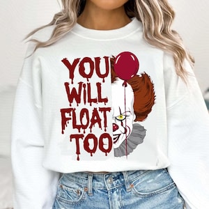 May include: White sweatshirt with a red graphic of a clown with a red balloon and the text "YOU WILL FLOAT TOO".