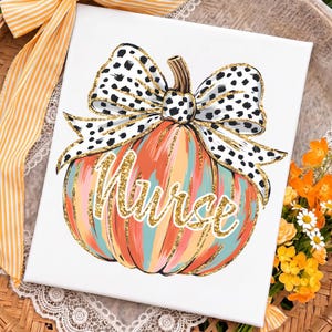 May include: A white canvas print featuring a painted pumpkin with vertical stripes in orange, teal, and pink. The pumpkin is topped with a large white bow featuring black spots and gold glitter edges. The word Nurse is written in gold glitter script.