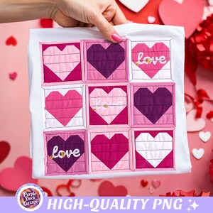 May include: White t-shirt featuring a patchwork design of nine heart-shaped blocks in shades of pink and purple. The word "love" is embroidered on three of the hearts. The shirt is held up by a hand.