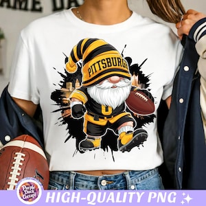 Puede incluir: Camiseta blanca con un gnomo de dibujos animados con un uniforme de fútbol negro y dorado, sosteniendo un balón de fútbol. El sombrero del gnomo dice "Pittsburgh". El diseño incluye un efecto de salpicadura negro y un horizonte de la ciudad. El texto "HIGH-QUALITY PNG" está en la parte inferior.