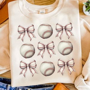 May include: A cream-colored sweatshirt with a repeating pattern of red and white baseballs and red and white bows.