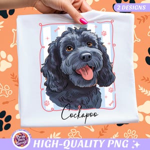 May include: White t-shirt featuring a Cockapoo dog illustration. The dog is black with brown eyes and a pink tongue. The design includes a pink frame with paw prints and bones. The text "Cockapoo" is written below the dog.