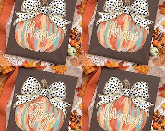 May include: A dark brown t-shirt featuring a graphic of a pumpkin with vertical stripes in orange, teal, and gold. The pumpkin is topped with a large white bow with black spots. The text Nana, Mimi, Gigi, or Mama is written in gold script.
