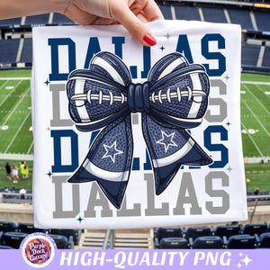Puede incluir: Una camiseta blanca con un gráfico grande de un lazo azul marino y blanco diseñado con textura de balón de fútbol y cordones blancos. La palabra DALLAS está impresa en letras grandes de bloque azul marino y gris detrás del lazo.