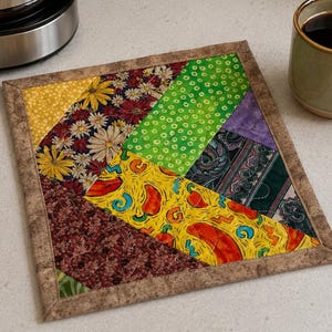 May include: A square quilted potholder featuring a patchwork design of various fabric patterns including yellow sunflowers, green polka dots, red chili peppers on yellow, and dark floral prints, all bordered by a solid brown textured fabric trim.