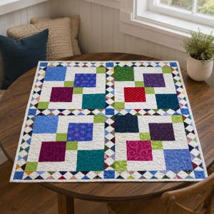 May include: A square patchwork quilt featuring a white background with a grid of large solid-colored squares in shades of blue, green, purple, red, and teal. The quilt is bordered by a repeating pattern of small multi-colored triangles.