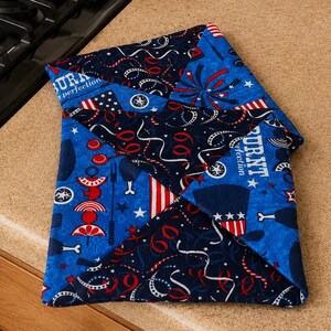 May include: A blue and red quilted oven mitt with a patriotic theme. The mitt features a patchwork design with fireworks, stars, and stripes. The text "BURNT perfection" is visible on the mitt.