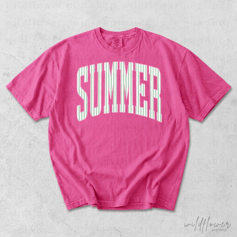 May include: A hot pink t-shirt with the word "SUMMER" printed across the front in large, white, vertical striped letters. The shirt has short sleeves and a crew neck.