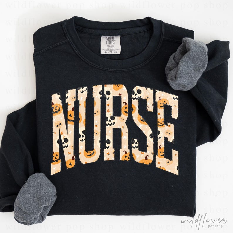 May include: A black long-sleeve sweatshirt featuring the word NURSE in large, block letters across the chest. The letters have a cream-colored background filled with a repeating pattern of orange jack-o'-lanterns and white skulls.