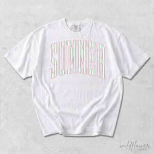May include: White t-shirt with the word "SUMMER" in a pink and green striped design across the front. The shirt has short sleeves and a crew neck. The Wildflower Pop Shop logo is in the bottom right corner.