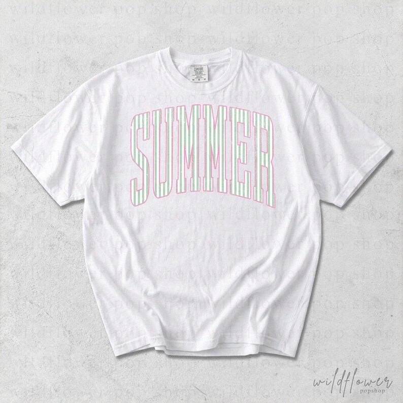 May include: White t-shirt with the word "SUMMER" in a pink and green striped design across the front. The shirt has short sleeves and a crew neck. The Wildflower Pop Shop logo is in the bottom right corner.