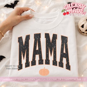 K&ouml;nnte beinhalten: Ein wei&szlig;es Sweatshirt mit Rundhalsausschnitt und dem Wort MAMA in gro&szlig;en, schwarzen Blockbuchstaben mit Used-Optik und Sternenmuster. Unter dem Text befindet sich eine kleine, pfirsichfarbene K&uuml;rbisgrafik, die auf den Stoff gedruckt ist.