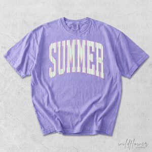 May include: A lilac-colored t-shirt with the word "SUMMER" printed across the front in a white and green striped design. The shirt has short sleeves and a crew neck.