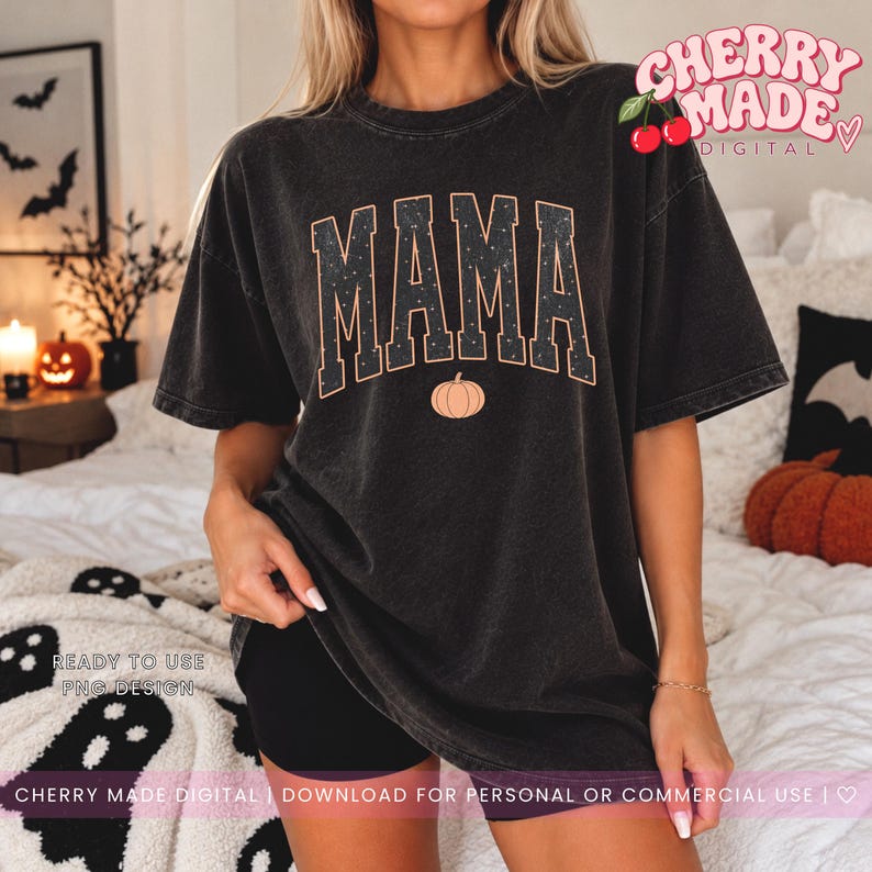 K&ouml;nnte beinhalten: Ein anthrazitfarbenes Kurzarm-T-Shirt mit dem Wort MAMA in gro&szlig;en Blockbuchstaben und einem dezenten Sternenmuster. Unter dem Text befindet sich eine kleine orangefarbene K&uuml;rbisgrafik. Das T-Shirt hat eine lockere Passform und ein Vintage-Finish.