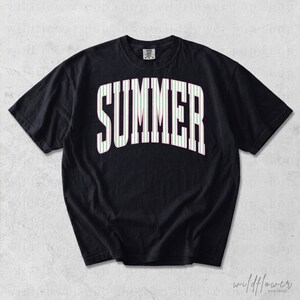May include: Black t-shirt with the word "SUMMER" in large, white, arched letters. The letters are filled with thin, vertical stripes of light green and pink. The shirt has short sleeves.