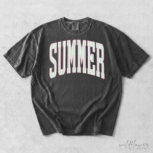 May include: A dark gray t-shirt with the word "SUMMER" in large white letters with green and pink stripes. The shirt has a vintage, washed look and a crew neck.
