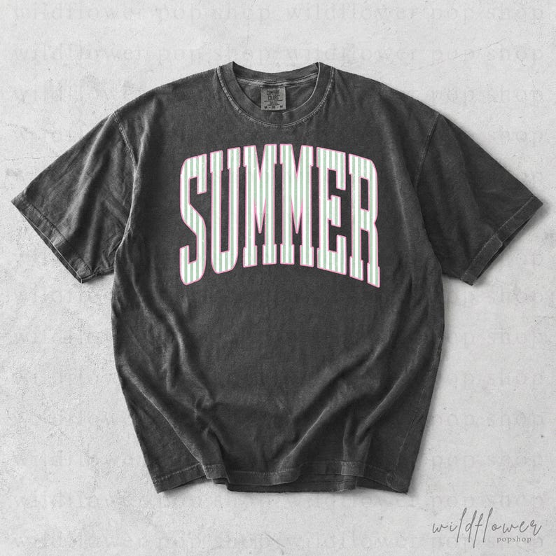 May include: A dark gray t-shirt with the word "SUMMER" in large white letters with green and pink stripes. The shirt has a vintage, washed look and a crew neck.