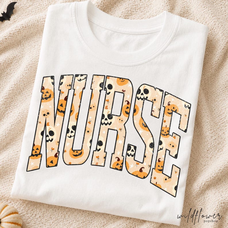 May include: A white short-sleeved t-shirt featuring the word NURSE in large block letters. The letters are filled with a repeating pattern of orange jack-o'-lanterns, white skulls, and small stars on a light beige background.