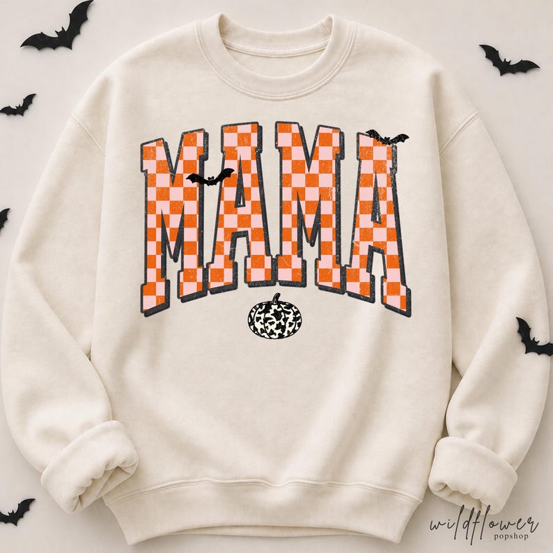 Puede incluir: Una sudadera de cuello redondo color crema con la palabra MAMA en una fuente universitaria grande a cuadros naranja y rosa claro. El dise&ntilde;o incluye peque&ntilde;as siluetas de murci&eacute;lagos negros y un gr&aacute;fico de calabaza con estampado de vaca.