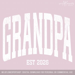 May include: A light pink graphic design featuring the word GRANDPA in large, distressed white capital letters with an arched layout. Below the text, the phrase EST 2026 is printed in white. The top right corner displays the text wildflower popshop.