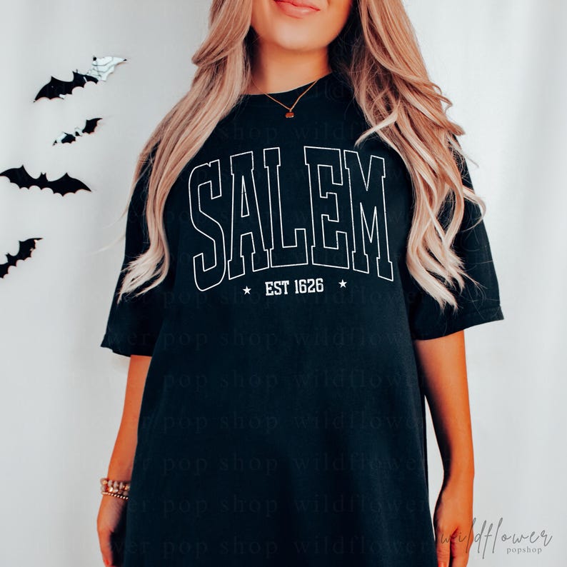 May include: A black short-sleeved t-shirt featuring the white outlined text SALEM in a collegiate font, with the text EST 1626 centered below it between two small stars. The shirt has a relaxed fit and a crew neckline.