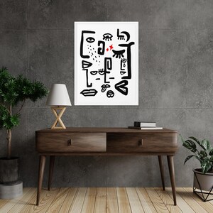 May include: Black and white abstract art print with a white background and black lines forming eyes, lips, and other facial features. The print is framed in a white frame and is hanging on a gray wall.