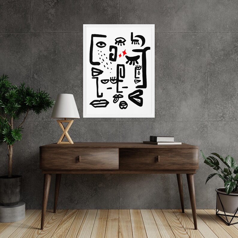 May include: Black and white abstract art print with a white background and black lines forming eyes, lips, and other facial features. The print is framed in a white frame and is hanging on a gray wall.