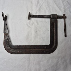 May include: A rusty metal C-clamp with a threaded screw and a handle. The clamp is open and ready to be used.
