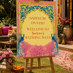 Può includere: Un cartello di benvenuto per matrimonio rettangolare su un cavalletto in legno con un centro giallo e il testo SADI KURI DA VIAH WELCOME TO Simran's WEDDING WEEK, incorniciato da bordi rosa e oro, pavoni blu e accenti floreali rosa.