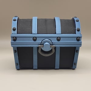 May include: A small, black wooden treasure chest with blue metal accents and a metal handle. The chest has a distressed wood finish and is decorated with metal studs.