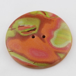 May include: A round, two-hole button with a marbled design in shades of orange, green, and pink.