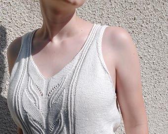 May include: A light gray, sleeveless knit top with a V-neck. The top features a cable knit design down the center and on the sides. The model is wearing sunglasses.