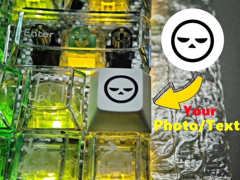 May include: A close-up of a keyboard with clear, green, and yellow keycaps. The keycaps have a variety of symbols and letters engraved on them. One keycap features a black and white graphic of a frowning face.
