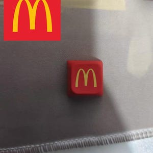 May include: A red square with a yellow "M" logo. The logo is the same as the McDonald's logo.