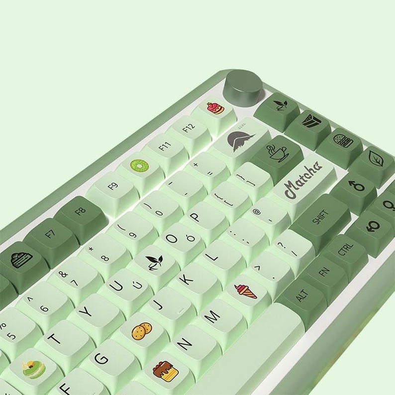 May include: A green and white keyboard with a light green background. The keys have various food-themed icons, including a kiwi, a cake, a donut, a leaf, a cup of tea, and an ice cream cone. The keyboard has the word "Matcha" printed on one of the keys.
