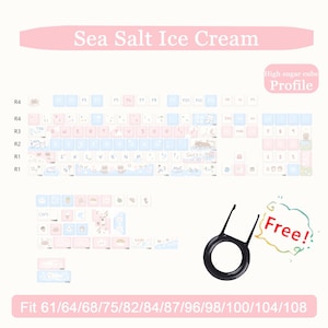 May include: A keyboard keycap set with a "Sea Salt Ice Cream" theme. The keycaps are light blue, pink, and white with cartoon illustrations. Includes a keycap puller and text that says "Free!" and "High sugar cube Profile".