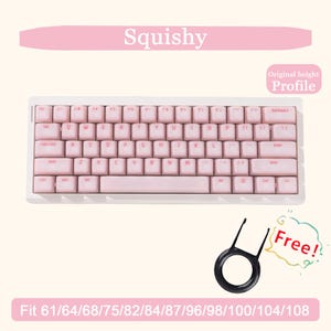 May include: A pink and white mechanical keyboard with pink keycaps. The keyboard has a white frame and includes a keycap puller. Text on the image reads "Squishy" and "Original height Profile". The keyboard is compatible with various sizes.