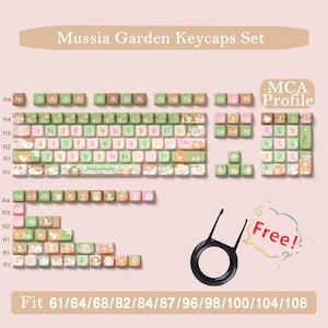 May include: A set of Mussia Garden keycaps in pastel green, pink, and peach. The keycaps feature a variety of illustrated designs and text. Includes a keycap puller. Compatible with 61/64/68/82/84/87/96/98/100/104/108 keyboards.