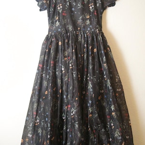 May include: A black floral print dress with a square neckline and short, scalloped sleeves. The dress features a fitted bodice and a full, flowing skirt. The fabric is semi-sheer, and the dress hangs on a black hanger.