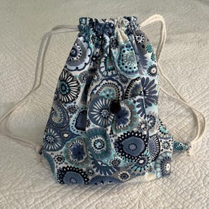 Op de afbeelding: Een blauwe en witte trekkoordtas met een bloemenpatroon. De tas heeft een klein vakje aan de voorkant.