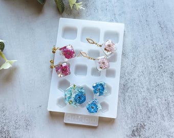 May include: A white silicone mold with 12 square cavities, used for making resin earrings. The mold is filled with resin earrings featuring pressed flowers in pink, white, and blue.