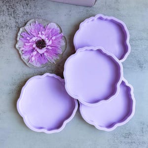 May include: Four lavender silicone moulds for making resin coasters. The moulds have a scalloped edge and are arranged in a stack.