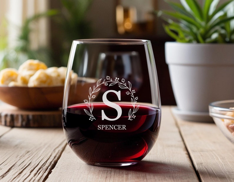 Peut inclure: Un verre &agrave; vin sans pied transparent avec un motif grav&eacute; blanc d'une couronne florale avec la lettre "S" au centre et le nom "Spencer" en dessous. Le verre est rempli de vin rouge.