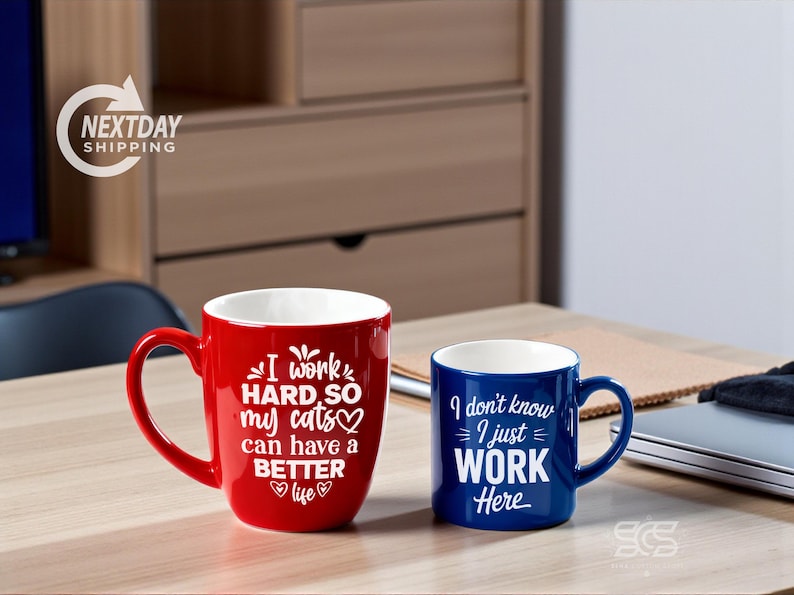 Pu&ograve; includere: Due tazze in ceramica su una superficie di legno. Una &egrave; rossa con il testo "I work HARD, SO my cats can have a BETTER life." L'altra &egrave; blu con il testo "I don't know I just WORK Here."