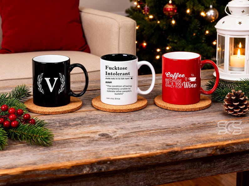 Pu&ograve; includere: Tre tazze in ceramica su sottobicchieri in sughero. Una tazza nera con una "V" bianca e un design a corona d'alloro, una tazza bianca con la scritta "Fucktose Intolerant" e una tazza rossa con la scritta "Coffee because it's too early for Wine".
