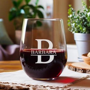 Peut inclure: Un verre &agrave; vin en verre transparent avec un pied et un large bol. Le verre est rempli de vin rouge. Le verre porte un monogramme blanc avec la lettre "B" et le nom "BARBARA" grav&eacute; dessus.