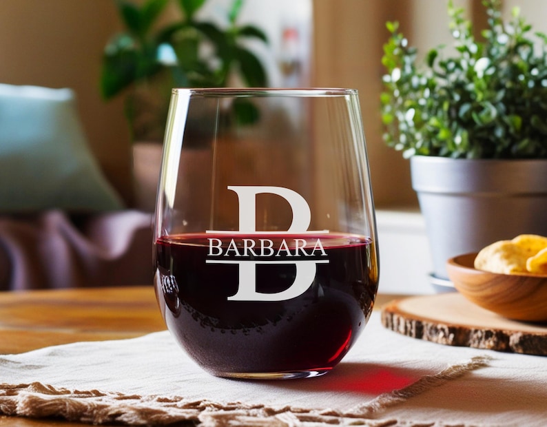 Peut inclure: Un verre &agrave; vin en verre transparent avec un pied et un large bol. Le verre est rempli de vin rouge. Le verre porte un monogramme blanc avec la lettre "B" et le nom "BARBARA" grav&eacute; dessus.