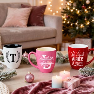 Pu&ograve; includere: Tre tazze in ceramica su un tavolo, perfette per i regali delle feste. Una &egrave; bianca con una "T" nera e un design a corona d'alloro, un'altra &egrave; rosa con una "L" floreale e il nome "Lauren", e la terza &egrave; rossa con la scritta "It's Just Water I Swear".
