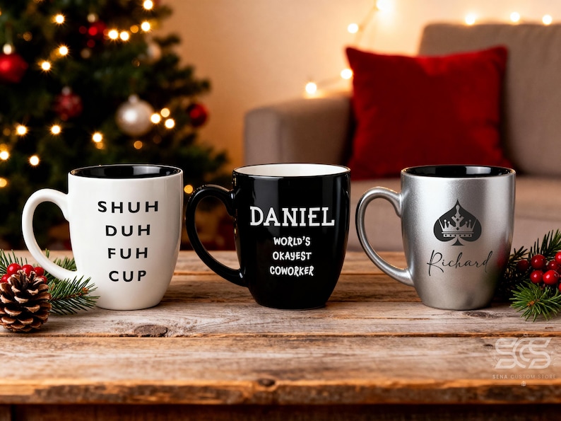Pu&ograve; includere: Tre tazze in ceramica con interni neri su una superficie di legno. Una &egrave; bianca con le parole "SHUH DUH FUH CUP". Un'altra &egrave; nera con "DANIEL WORLD'S OKAYEST COWORKER". La terza &egrave; argentata con un disegno di picche e il nome "Richard".