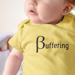 May include: A yellow baby onesie with the word "Buffering" printed in black. The onesie is short-sleeved and has a round neckline. The baby is wearing a small stud earring.